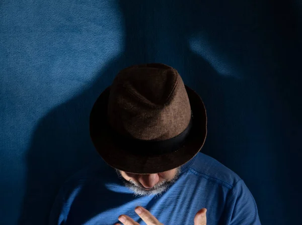 Stock image Studio portrait of man wearing hat with head down and gesticulating. Isolated on blue background.