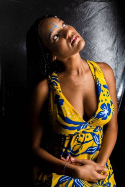 Siyah kadın, yukarı bakıyor, saçlarında uzun örgüler ve yüz boyalarıyla. Gümüş arka planda izole edilmiş.