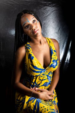 Siyah kadın, yukarı bakıyor, saçlarında uzun örgüler ve yüz boyalarıyla. Gümüş arka planda izole edilmiş.