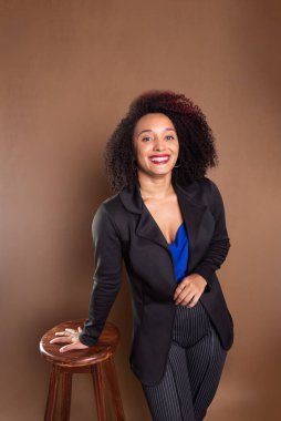 Genç yönetici, zarif ve güzel, tahta bir tabureye yaslanıyor. Başarı konsepti.