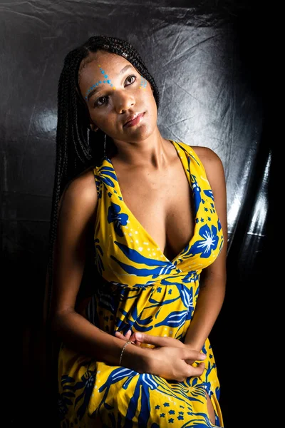 Siyah kadın, yukarı bakıyor, saçlarında uzun örgüler ve yüz boyalarıyla. Gümüş arka planda izole edilmiş.