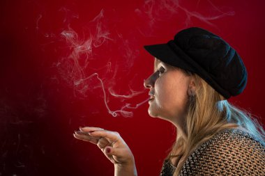 Çekici ve güzel bir kadının el kaldırılmış ve tütsü dumanı üfleyen stüdyo portresi. Kırmızı arkaplanda izole edilmiş.