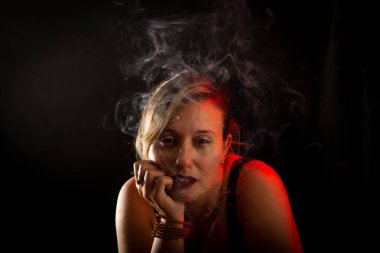 Çekici ve güzel sakin bir kadın elleri yüzünde kameraya bakıyor. Tütsü dumanı her yerde. Stüdyo portresi. Siyah bir arkaplanda izole edilmiş.