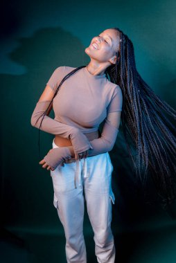 Güzel genç bir kadın saç örgülerini sallıyor. Koyu renkli arkaplanda izole edilmiş.