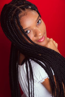 Uzun örgülü, kendine güvenen ve gülümseyen güzel bir genç kadın. Kırmızı arkaplanda izole.