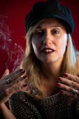Siyah bereli çekici ve kendine güvenen bir kadın. Tütsü dumanı her yerde. Kırmızı arkaplanda stüdyo portresi.