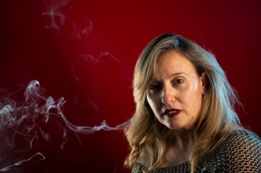 Çekici, kendine güveni tam bir kadın. Etrafında tütsü dumanıyla kameraya bakıyor. Kırmızı arkaplanda izole edilmiş.