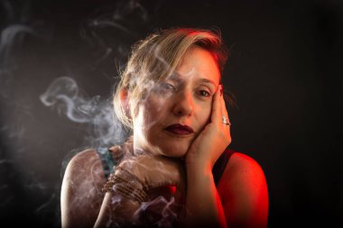 Çekici ve güzel bir kadın, eli hafifçe yüzüne dokunuyor. Tütsü dumanı her yerde. Stüdyo portresi. Siyah bir arkaplanda izole edilmiş.