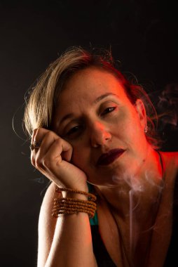 Çekici ve güzel sakin bir kadın elleri yüzünde kameraya bakıyor. Tütsü dumanı her yerde. Stüdyo portresi. Siyah bir arkaplanda izole edilmiş.