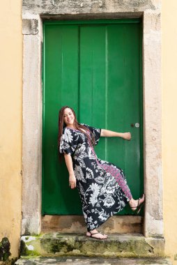 Yeşil renkli bir kapıya yaslanmış kameraya bakan bir kadın. Mutlu ve kendinden emin kişi.