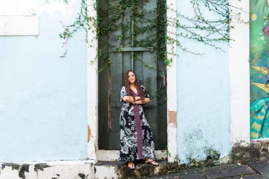Yeşil bir kapıya karşı duran güzel bir kadın ve yeşil bitkilerle dolu mavi bir duvar. Seyahatte bir turist. Pelourinho, Brezilya.