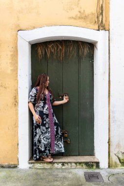 Renkli elbiseli güzel bir kadın yeşil renkli bir kapının asma kilidini tutuyor. Seyahatte bir turist. Pelourinho, Brezilya.