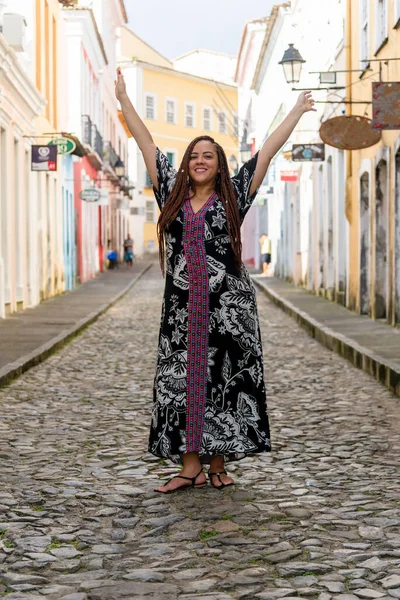 Pelourinho 'nun eski kaldırım taşı sokağında saçları örgülü bir turist olarak duran güzel bir kadının portresi. Arka planda eski evler var. Salvador, Brezilya.
