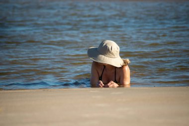 Bikinili ve şapkalı bir kadın denizin sularında yatıyor. Taquari, Guaibim plajı, Valenca, Bahia.