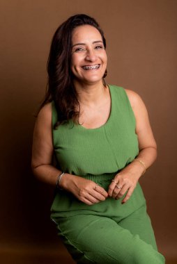 Yeşil elbiseli güzel bir kadının portresi. Güven, motivasyon ve olgunluk kavramı. Kahverengi arkaplanda izole.