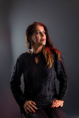 Güzel ve çekici bir kadın kendinden emin ve kendinden emin oturuyor. Stüdyo fotoğrafı. Koyu gri arka planda izole edilmiş.