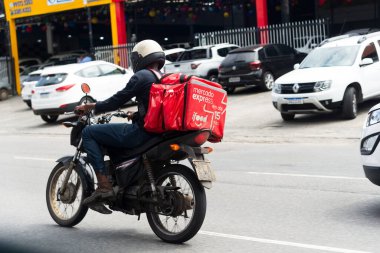 Salvador, Bahia, Brezilya - 11 Ağustos 2023: İffet uygulamasını kullanan bir gıda dağıtım görevlisi Salvador, Bahia 'da Avenida Bonoco' da motosikletine binerken görüldü.,