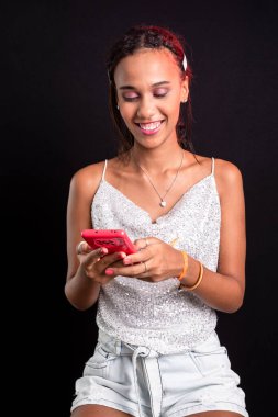 Gülümseyen bir gencin portresi. Cep telefonu kullanıyor ve bakıyor. Siyah arkaplanda izole.