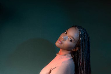 Saçında örgülerle kameraya bakan güzel bir genç kadının stüdyo portresi. Koyu renkli arkaplanda izole edilmiş.