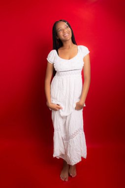 Uzun beyaz giysiler içinde ayakta duran güzel genç bir kadın. Kırmızı arkaplanda izole.