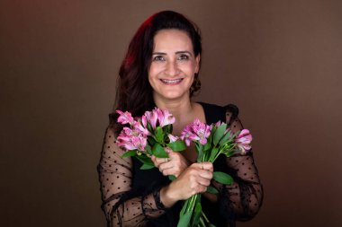 Siyah elbiseli güzel bir kadın elinde bir buket çiçek tutuyor. Aşık ve mutlu. Kahverengi arkaplanda izole.