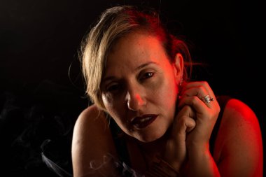 Çekici ve güzel bir kadın, eli hafifçe yüzüne dokunuyor. Tütsü dumanı her yerde. Stüdyo portresi. Siyah bir arkaplanda izole edilmiş.