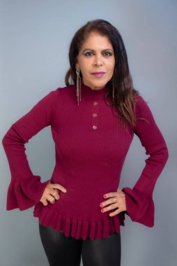 Güzel, olgun, çekici esmer, siyah pantolon ve kırmızı bluz giymiş, ayakta duran bir portre. Stüdyo fotoğrafı. Koyu gri arka planda izole edilmiş.