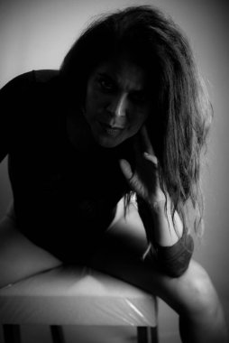 Seksi pozlarda oturan esmerin siyah beyaz portresi. Stüdyo fotoğrafı. Koyu arkaplan.