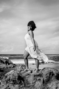 Siyah beyaz bir taş üzerinde siyah saçlı güzel bir kadının portresi. Arka planda gökyüzü ve deniz. Rio Vermelho, Salvador, Brezilya.