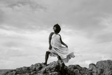 Siyah beyaz bir taş üzerinde siyah saçlı güzel bir kadının portresi. Arka planda gökyüzü ve deniz. Rio Vermelho, Salvador, Brezilya.