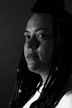 Saçında örgüler ve yüzünde geometrik gölgeler olan güzel bir kadının siyah beyaz portresi. Siyah arkaplan ile stüdyo portresi.