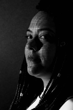 Saçında örgüler ve yüzünde geometrik gölgeler olan güzel bir kadının siyah beyaz portresi. Siyah arkaplan ile stüdyo portresi.