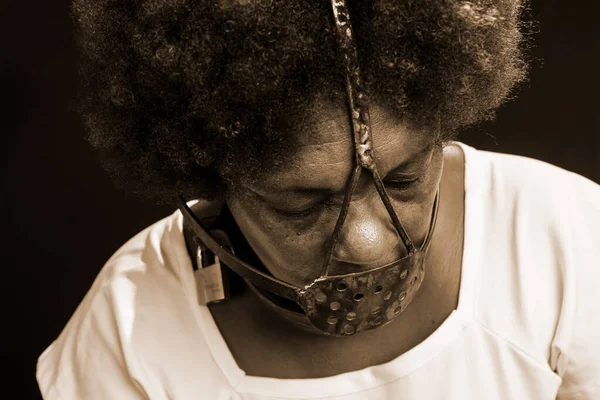 Portrait of the face of a black woman with an iron mask on her face, representing the slave Anastacia. Pain and suffering, torture. Against black background.