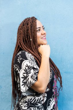 Saçları örgülü, yana bakan bir kadın. Mavi bir duvarda izole edilmiş..