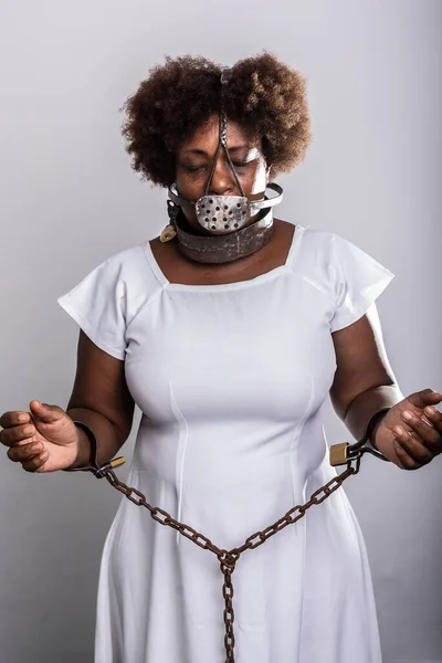Portrait of a black woman in chains with an iron mask over her mouth. Slavery in Brazil. Arms in prayer. Studio reproduction.