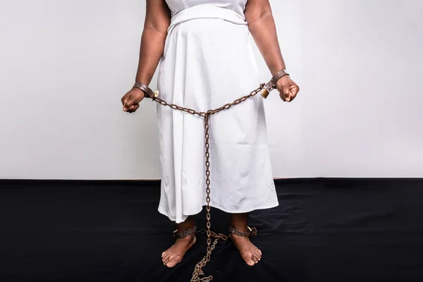 Hands and legs of a black woman chained with old rusty iron chain and padlock. Slave trade prevention concept.