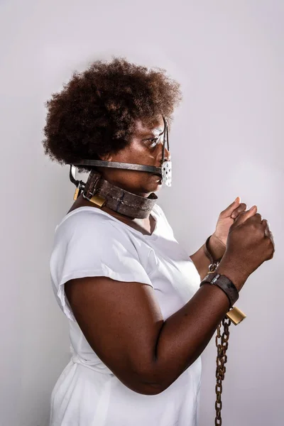 Portrait of sad woman trapped with old rusty chains and mask on her face. Hands in prayer asking for help. Slave trade prevention concept.