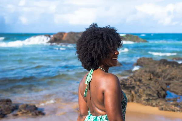 Portrait of woman with black power hair looking at the sea. In the background the sky rocks and the sea. Rio Vermelho Beach, Salvador, Brazil.