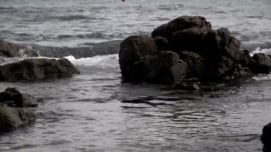 Deniz dalgaları güneşli bir günde kumsalın siyah kayalarına çarpıyor. Rahatlama hissi..