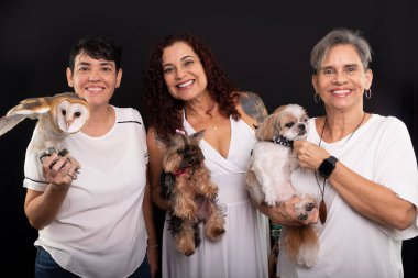 Evcil hayvanlarıyla mutlu, kendinden emin üç lezbiyen kadın. Bir baykuş, Yorkshire ve Shih Tzu köpekleri. Siyah arkaplana karşı stüdyo görüntüsü.