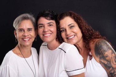 Üç kadının stüdyo fotoğrafı, lezbiyenler, mutlu ve özgür bir şekilde kameraya bakıyorlar. Siyah arkaplanda izole.