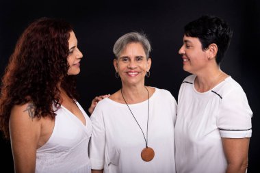 Üç güzel kadın, lezbiyenler, arkadaşlar kameraya mutlu ve komik poz veriyorlar. Siyah arka planda izole edilmiş. Siyah arkaplana karşı stüdyo portresi.