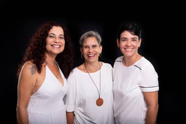 Üç kadının stüdyo fotoğrafı, lezbiyenler, mutlu ve özgür bir şekilde kameraya bakıyorlar. Siyah arkaplanda izole.