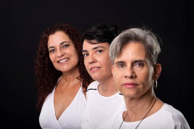 Üç güzel kadının portresi, lezbiyenler, müzisyen arkadaşlar ve kameraya poz verirken mutlu olmak. Siyah arkaplana karşı stüdyo görüntüsü.