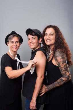 Üç güzel kadının portresi, arkadaşlar, siyah kıyafetler giyen bir müzik grubunun üyeleri. Gri arkaplanlı stüdyo fotoğrafı.