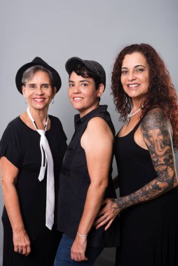 Üç güzel kadının portresi, arkadaşlar, siyah kıyafetler giyen bir müzik grubunun üyeleri. Gri arkaplanlı stüdyo fotoğrafı.