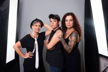 Üç güzel kadının portresi, arkadaşlar, siyah kıyafetler giyen bir müzik grubunun üyeleri. Gri arkaplanlı stüdyo fotoğrafı.