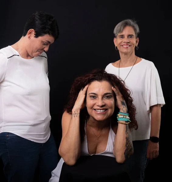 Three beautiful women, one sitting and two standing, musician lesbians friends and happy against black background in studio.