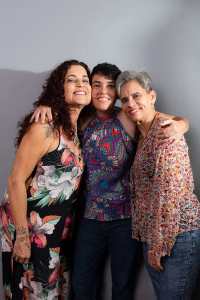 Three beautiful female musicians wearing colorful clothes, hugging each other in a gesture of affection, respect and friendship. Leaning against gray color background in studio.