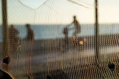 Bisikletçilerin silueti ve gün batımına karşı sahilde yürüyen insanlar. Fiziksel egzersizler ve zihnin rahatlaması..